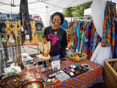 woman poses behind table of her vendor shop of jewelry and clothes