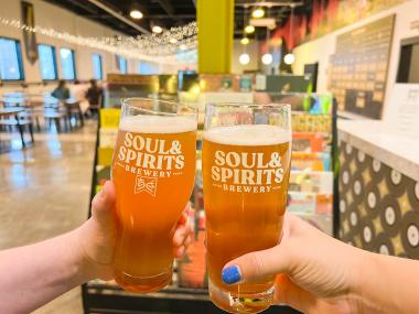 two beers being held in cheers with brewery name on them