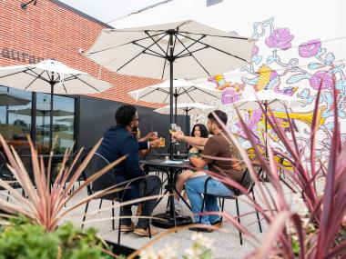 Four friends sitting on the outdoor patio toasting drinks at JEM.