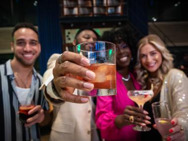 four friends hold up cocktails and smile for photo
