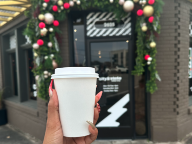 coffee held up in front of City &amp; State doorway that is decorated for the holidays