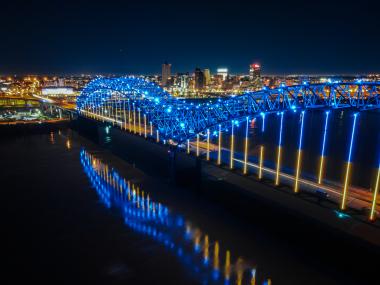 memphis "M" bridge lit up blue at night with city skyline in background