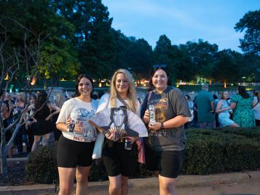 three women pose for photo with elvis memorabilia at candlelight vigil at Graceland