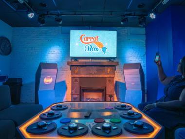 view from couch in game nite lounge with control panel, tv on wall and two game show stands