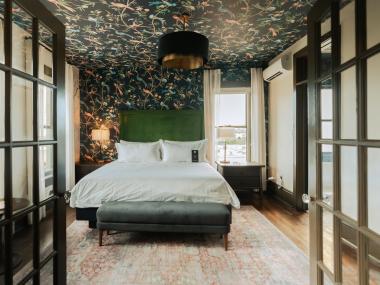 doors open into suite hotel room of Hotel Pontotoc with bed, wallpaper on back wall and ceiling