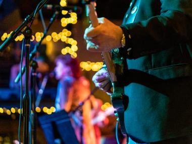 close up of man playing guitar with holiday lights in background